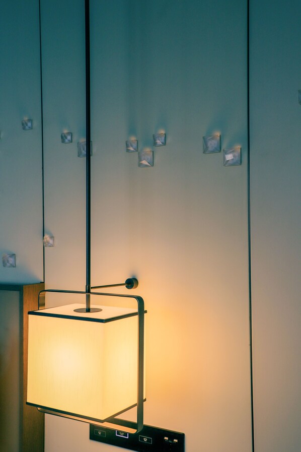A modern interior with a hanging square-shaped lamp, a wall-mounted control panel, and lockers.
