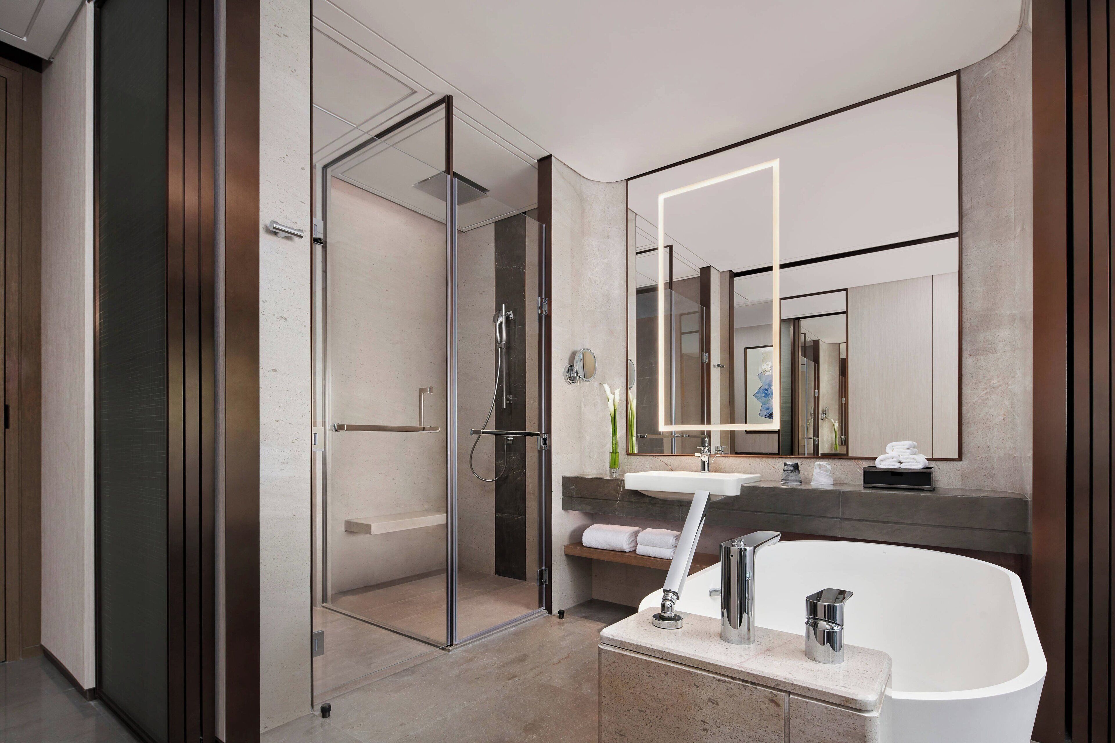 Un baño moderno con ducha envuelta en vidrio, una bañera independiente y un espejo grande sobre el lavabo.