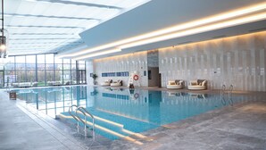 A modern indoor swimming pool with clear glass walls, lounge chairs, and a well-lit ceiling. - Yancheng Marriott Hotel (Yancheng)