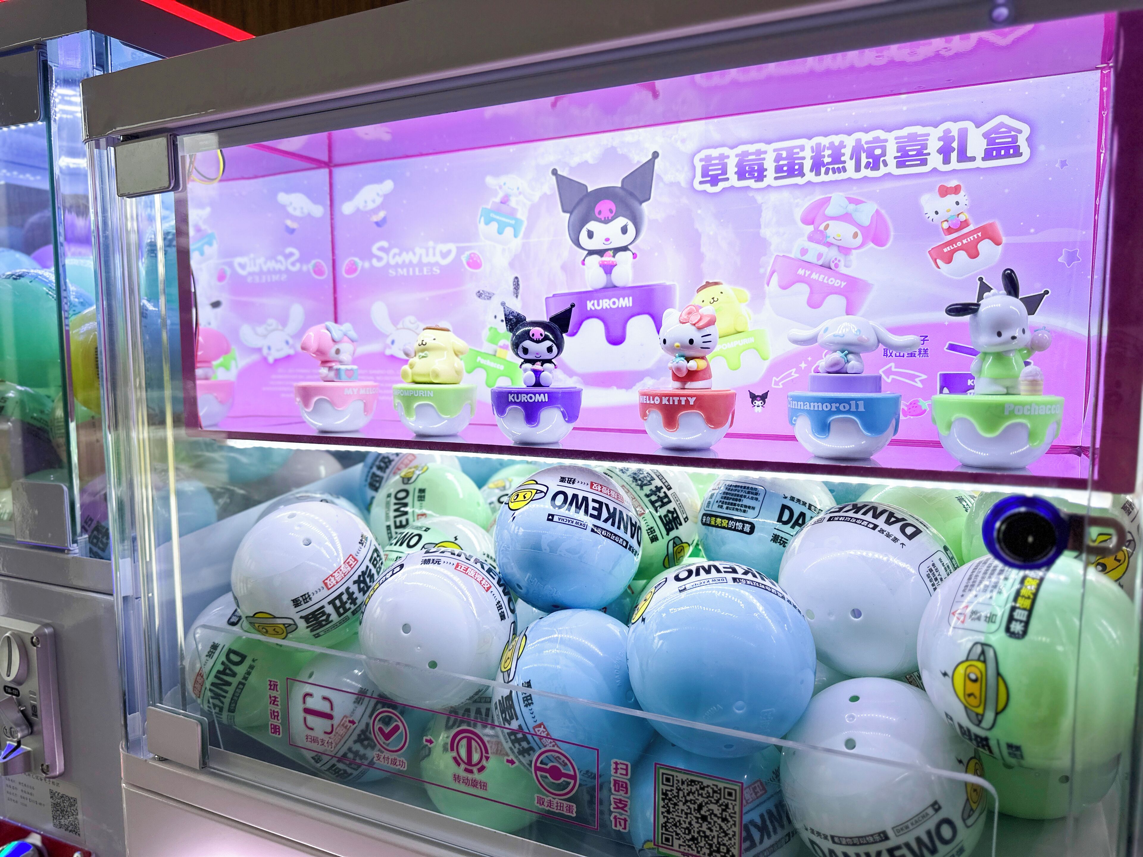 A claw machine filled with colorful balls and a display featuring Hello Kitty and other characters.