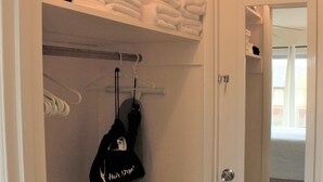 Ein Schrank mit ordentlich gefalteten Handtüchern, einem aufgehängten Kleidungsstück und einer Tür zu einem anderen Raum.