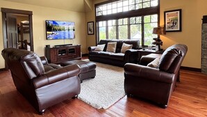 A spacious living room with leather sofas, a flat-screen TV, and large windows offering natural light.