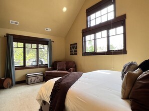 A bedroom with a large bed, a sofa, a window with curtains, and a small table.