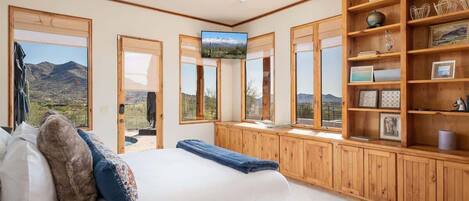A bedroom with a bed, wooden shelves, a television, and large windows with a mountain view.
