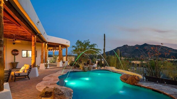 A pool with a waterfall feature, surrounded by rocks and potted plants, with a view of mountains in the background.