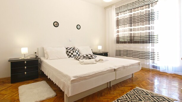 A bedroom with a large bed, two bedside tables, a nightstand, a white rug, and a patterned rug.