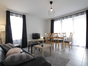 Un salon moderne comprenant un canapé, une table basse, un téléviseur et un coin repas avec des chaises et une table.