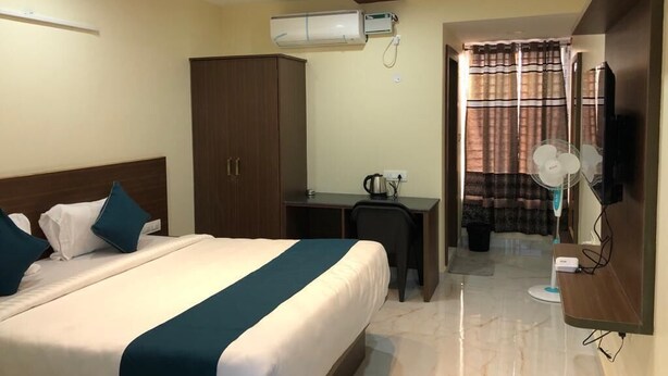 Habitación de hotel con cama, escritorio, aire acondicionado, ventilador y televisor.