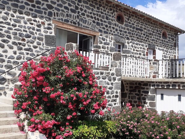 A stone building with a balcony and a large bush of pink flowers.
