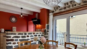 Un coin repas avec un mur en pierre, une table en bois, des chaises, un vase avec des fleurs, une horloge et un téléviseur fixé au mur.