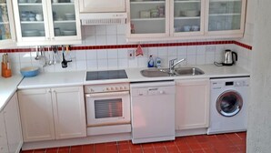 Eine kompakte Küche mit weißen Schränken, einem Backofen, einem Geschirrspüler und einer Waschmaschine.