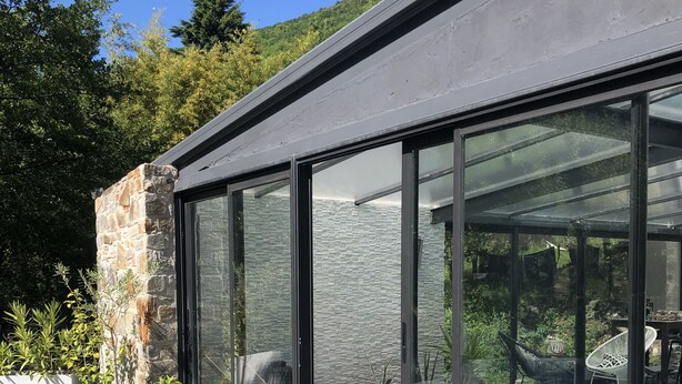 A modern outdoor pool area with a glass enclosure, stone wall, and outdoor furniture. - Villa sur la Route des Châteaux Cathares (Miraval-Cabardes)