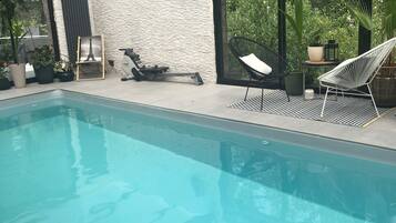 Une piscine intérieure à l’eau claire, entourée de chaises longues modernes et de plantes en pot.