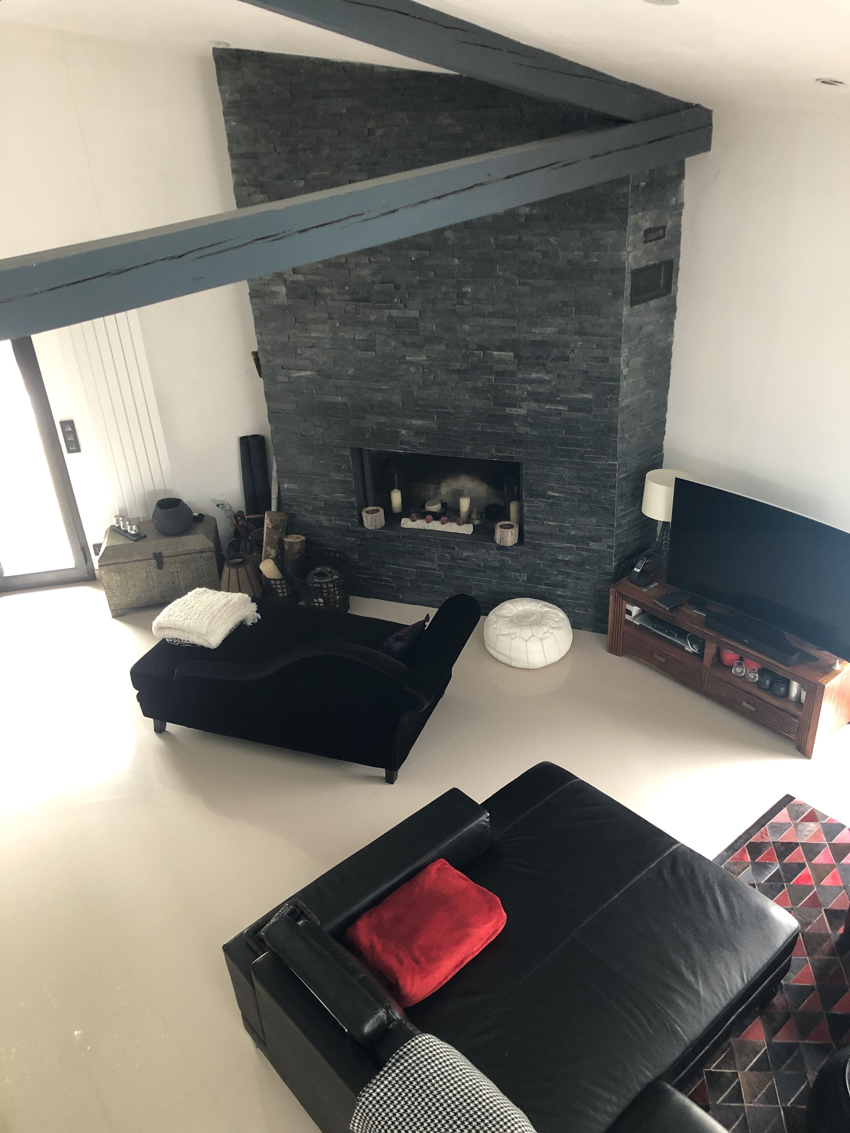 Una sala moderna con chimenea de piedra, sofás negros, un mueble para televisión y un reposapiés estampado.