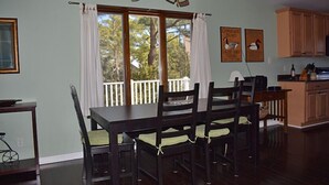 Een eetruimte met een tafel en stoelen, een plafondventilator, een raam met gordijnen en uitzicht op bomen.