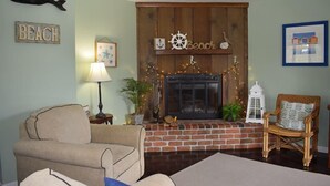Een woonkamer met een open haard, een bank, een fauteuil en een muur met een bordje 'Beach'.