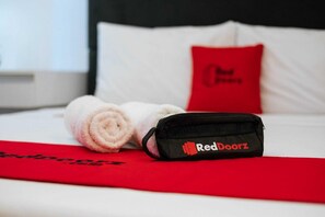 Un letto rifatto con cura, un asciugamano arrotolato e una borsa nera con il marchio 'RedDoorz'.