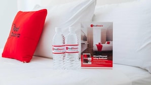 A bed with white bedding, a red pillow, and two RedDoorz water bottles. - Reddoorz @ Camaman-an Cagayan De Oro City (Cagayan de Oro)