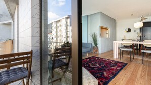A modern apartment with a balcony, a dining area with a table and chairs, and a living room with a sofa and a rug.