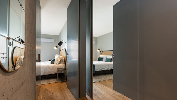 A modern bedroom with two beds, wooden flooring, and a large mirror.