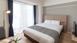 Et moderne hotelværelse med en stor seng, et skrivebord med en bærbar computer, et fjernsyn og et vindue med gardiner.