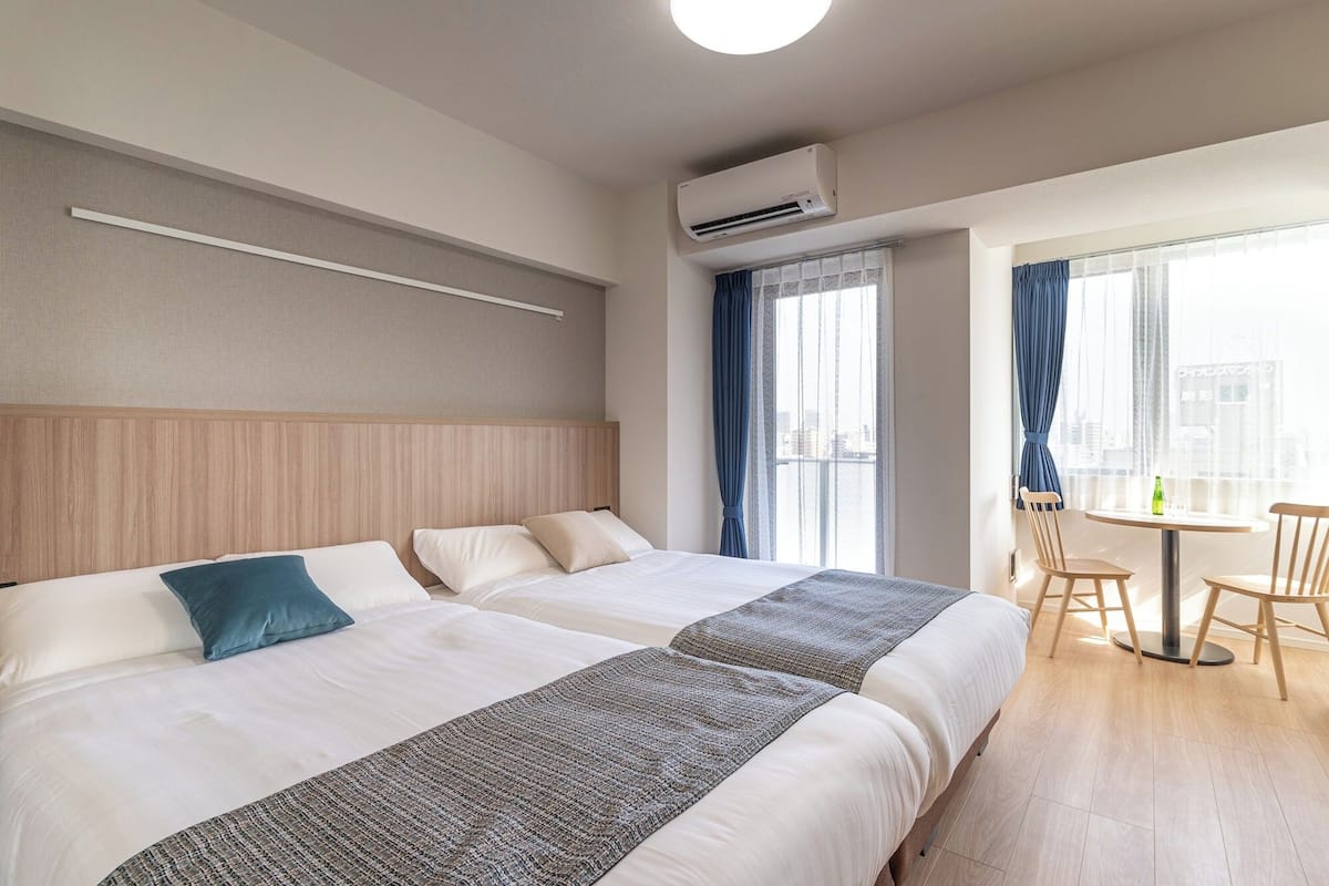 Habitación de hotel con dos camas, un comedor y vista a la ciudad.
