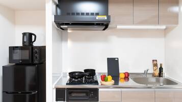 A modern kitchen with a built-in microwave, stove, and oven, a sink, and a small countertop with fruits and a cutting board.