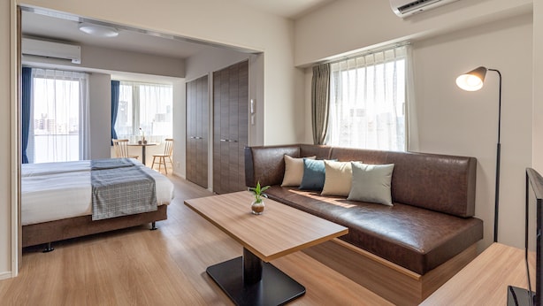 Et moderne hotelværelse med en seng, et træ sofabord, en brun lædersofa og et fjernsyn.