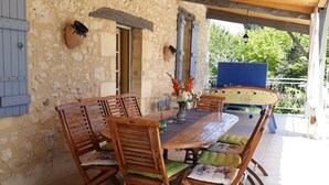 A wooden dining table with chairs, a vase of flowers, and a blue boat in the background. - Charming Farmhouse with Private Pool, Garden, and Playground in Peaceful Countryside (Rampieux)