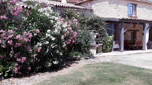 A house with a covered patio and a garden with flowering plants. - Charming Farmhouse with Private Pool, Garden, and Playground in Peaceful Countryside (Rampieux)