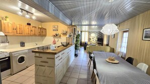 A modern kitchen with wooden cabinets, a built-in washing machine, and a dining area with a table and chairs. - Charming Farmhouse with Private Pool, Garden, and Playground in Peaceful Countryside (Rampieux)