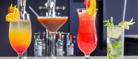 Four cocktails on a bar counter with a blurred background of bar equipment.