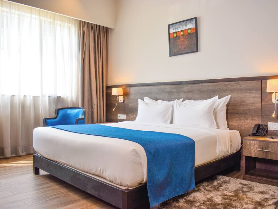 A hotel room with a large bed, a chair, a nightstand with a phone, and a painting on the wall.