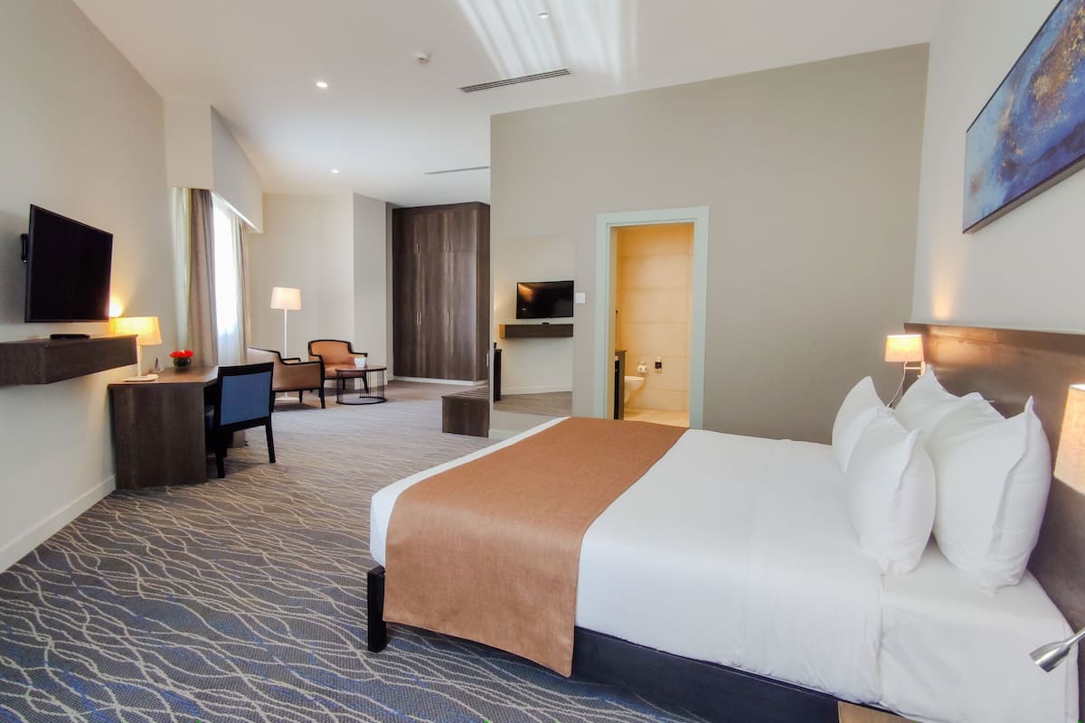 Una habitación de hotel con una cama grande, un escritorio con silla, televisión y un baño visible a través de una puerta abierta.