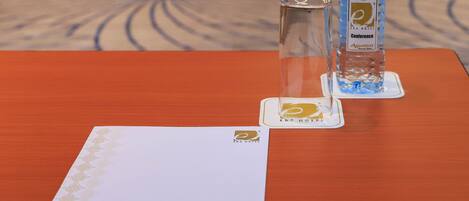 A hotel room with a wooden table, a glass, a bottle of water, and a card with the hotel logo.