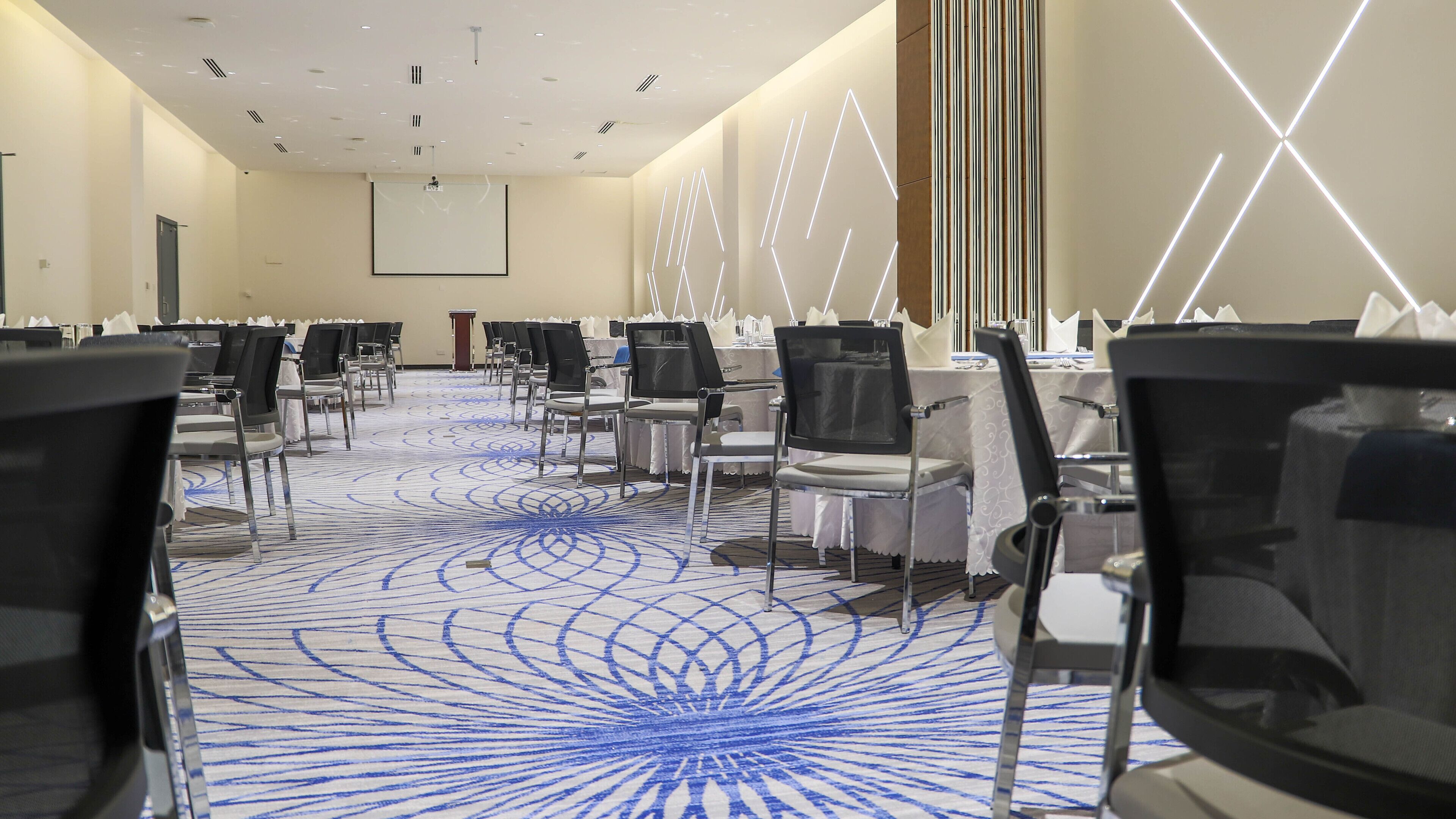 A conference room with rows of chairs, a projector screen, and a patterned carpet.