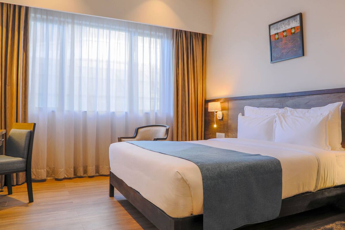 Una habitación de hotel con una cama, una silla, un escritorio y un ventanal con cortinas.