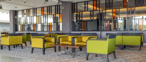 A modern interior with yellow chairs, a patterned carpet, and large windows with orange lighting.