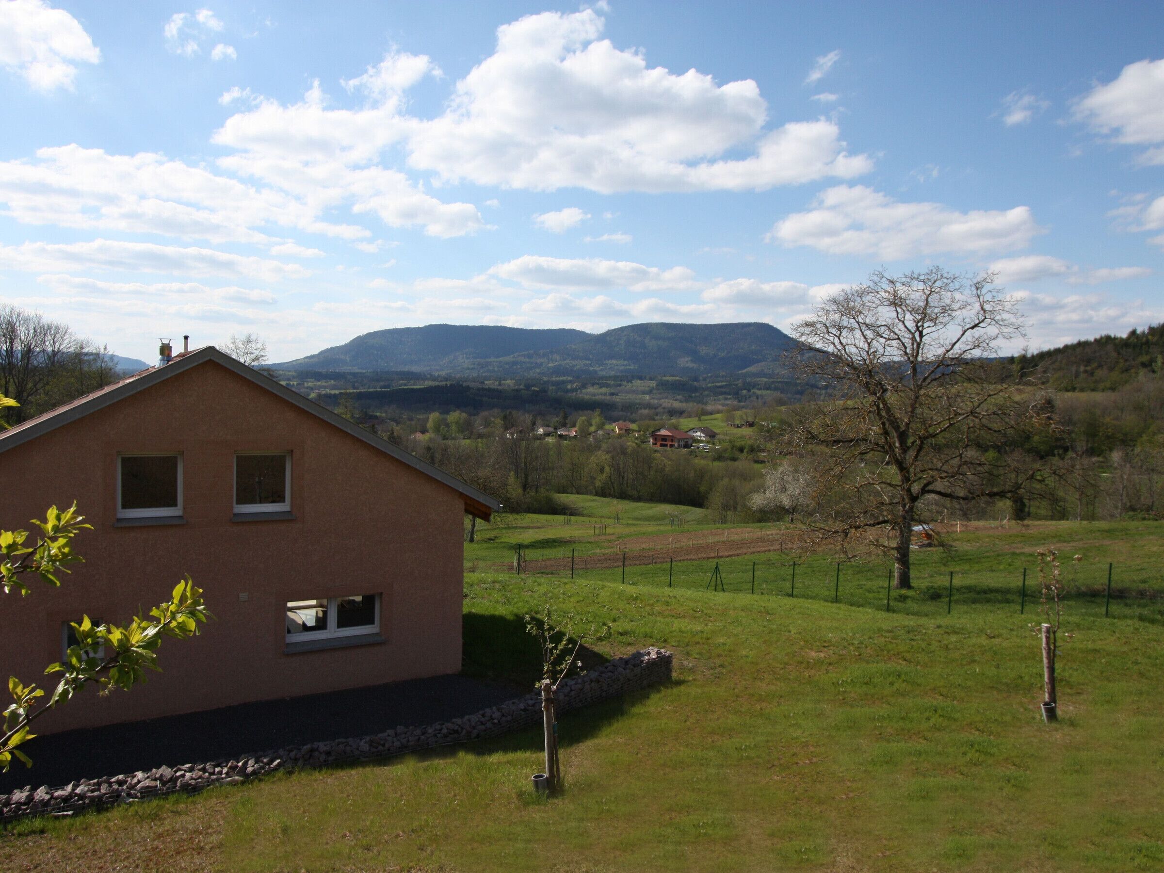 Une maison de plain-pied avec un toit en pente, des fondations en pierre et une cour clôturée.