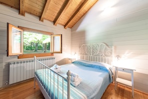 A bedroom with a metal bed frame, a window with a view of trees, a radiator, and a bedside table. - Villa Degli Ulivi, With Large Garden and Swimming Pool (Civitella del Tronto)