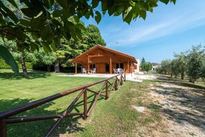 A wooden cabin with a covered patio, surrounded by trees and a grassy area. - Villa Degli Ulivi, With Large Garden and Swimming Pool (Civitella del Tronto)