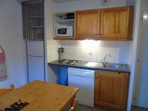 Una cocina compacta con armarios de madera, microondas, lavaplatos y lavadero.