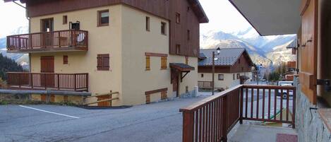 A building with a balcony, a road in front, and mountains in the background.