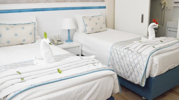 A hotel room with two beds, a nightstand, a lamp, and a bathroom visible in the background. - A Warmly Welcome Home to Star Holiday Hotel 34 (Istanbul)