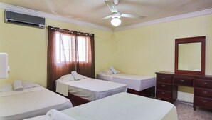Une chambre d’hôtel avec deux lits simples, une commode en bois, un miroir et un appareil de climatisation.