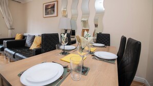 A dining area with a table set for four, a black leather sofa, and a mirror with a wavy design on the wall. - Fantastic 4 bed house with 3 bathrooms in pleasant location (West Bromwich)