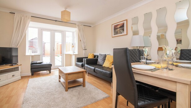 A modern living room with a TV, sofa, dining table, and a large window. - Fantastic 4 bed house with 3 bathrooms in pleasant location (West Bromwich)