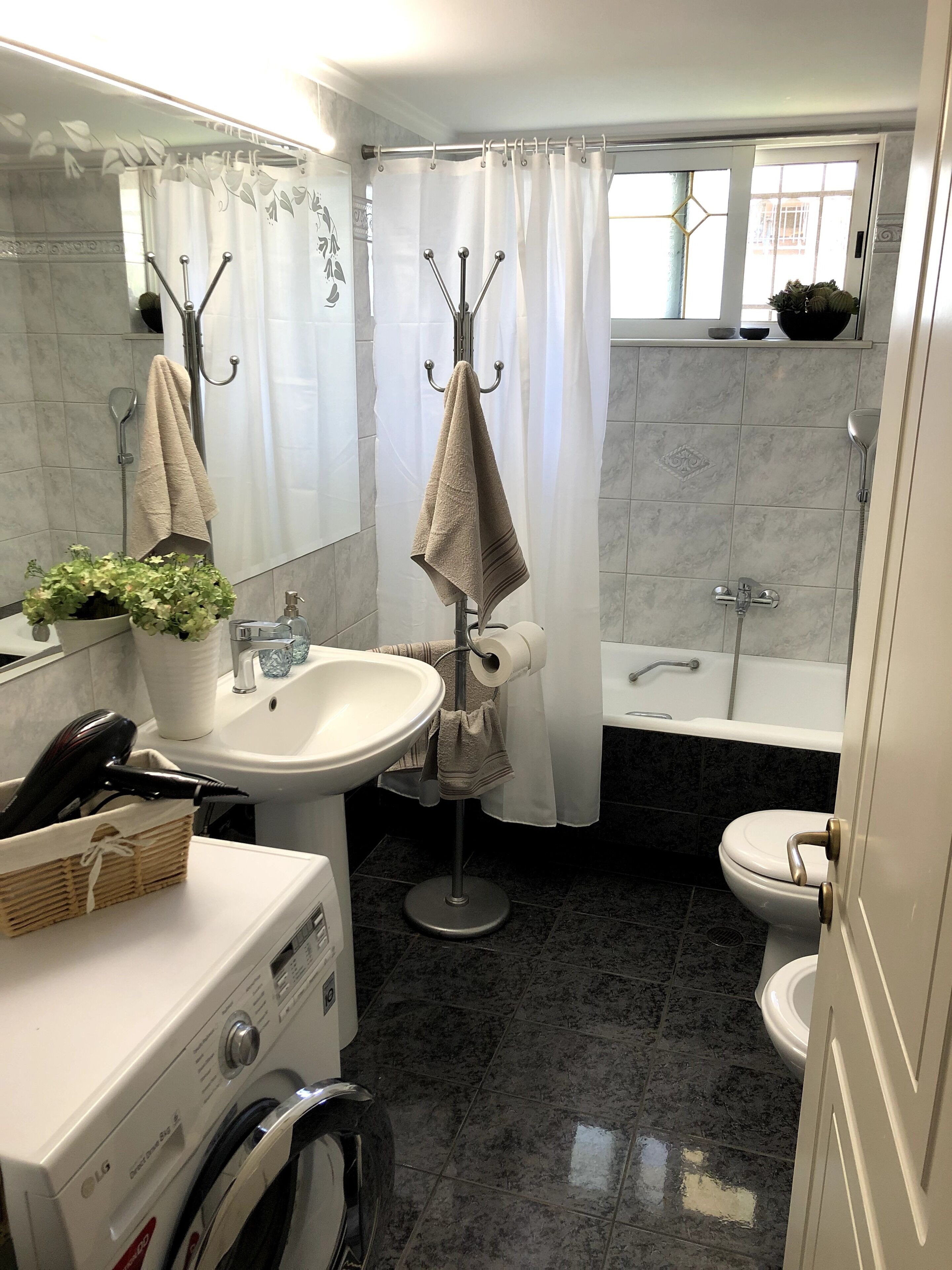 A bathroom with a sink, mirror, towel rack, shower, toilet, and a washing machine.
