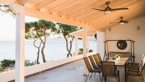 A covered outdoor dining area with a view of the sea, wooden ceiling, and ceiling fans.