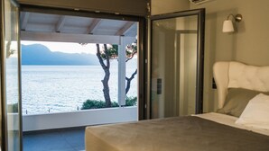 A bedroom with a bed, a window, and a view of a body of water and mountains.